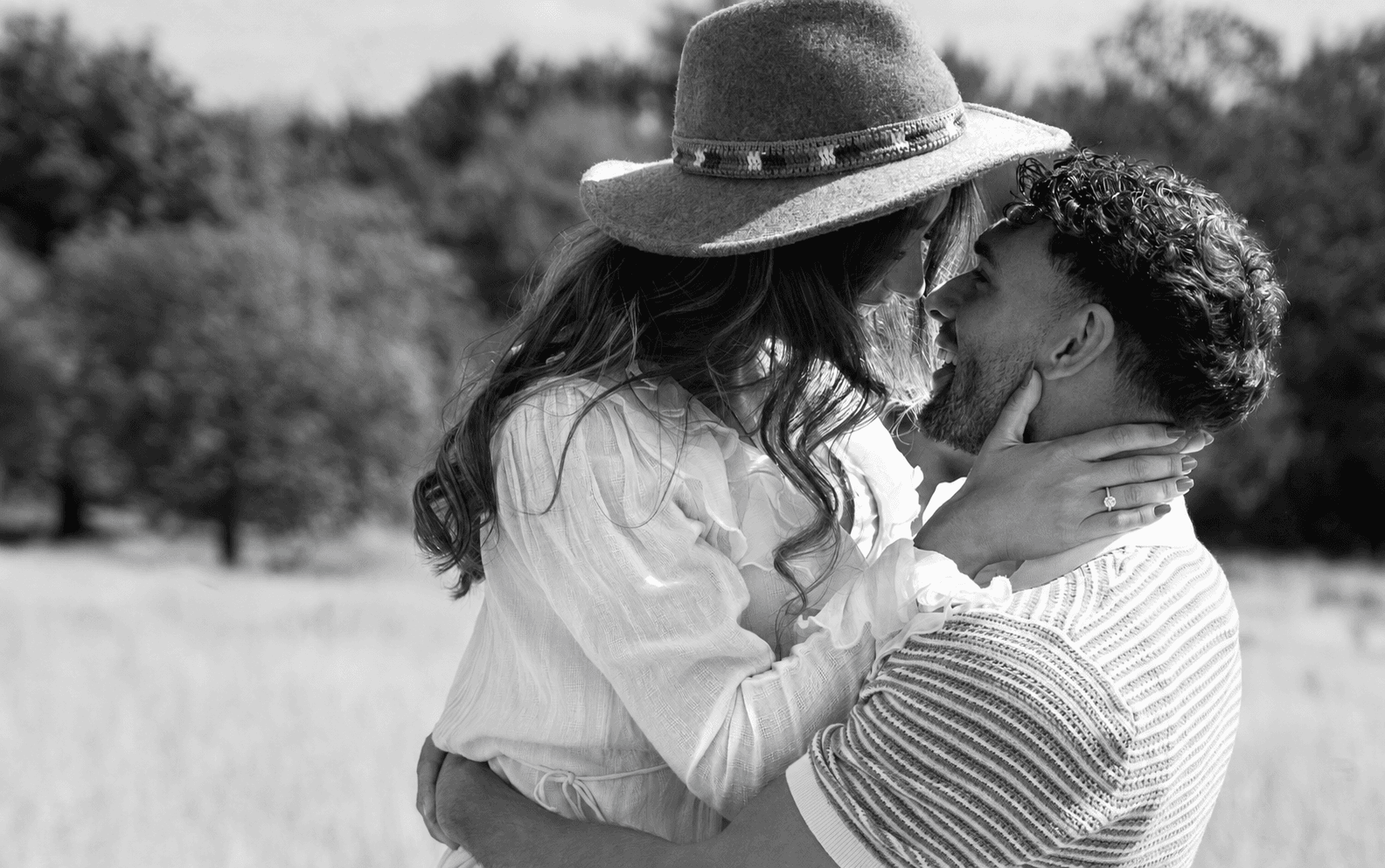 A couple embracing in a summer meadow, her engagement ring on show