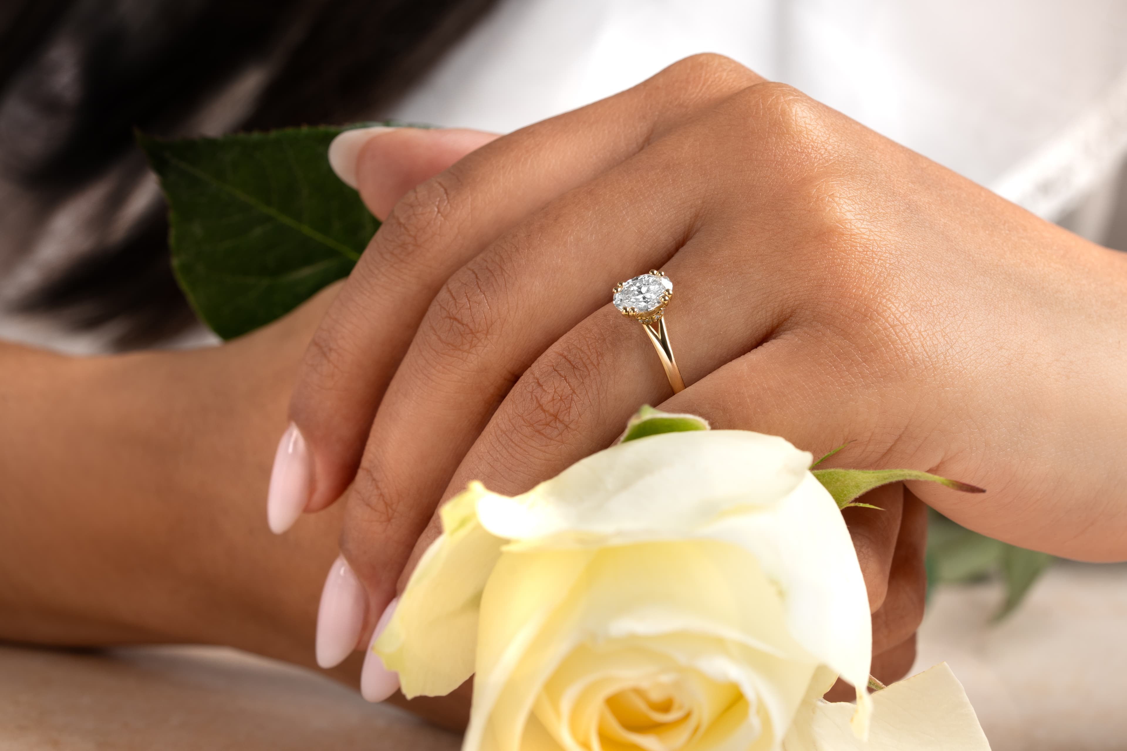 A hand wearing a handcrafted engagement ring resting on a white rose
