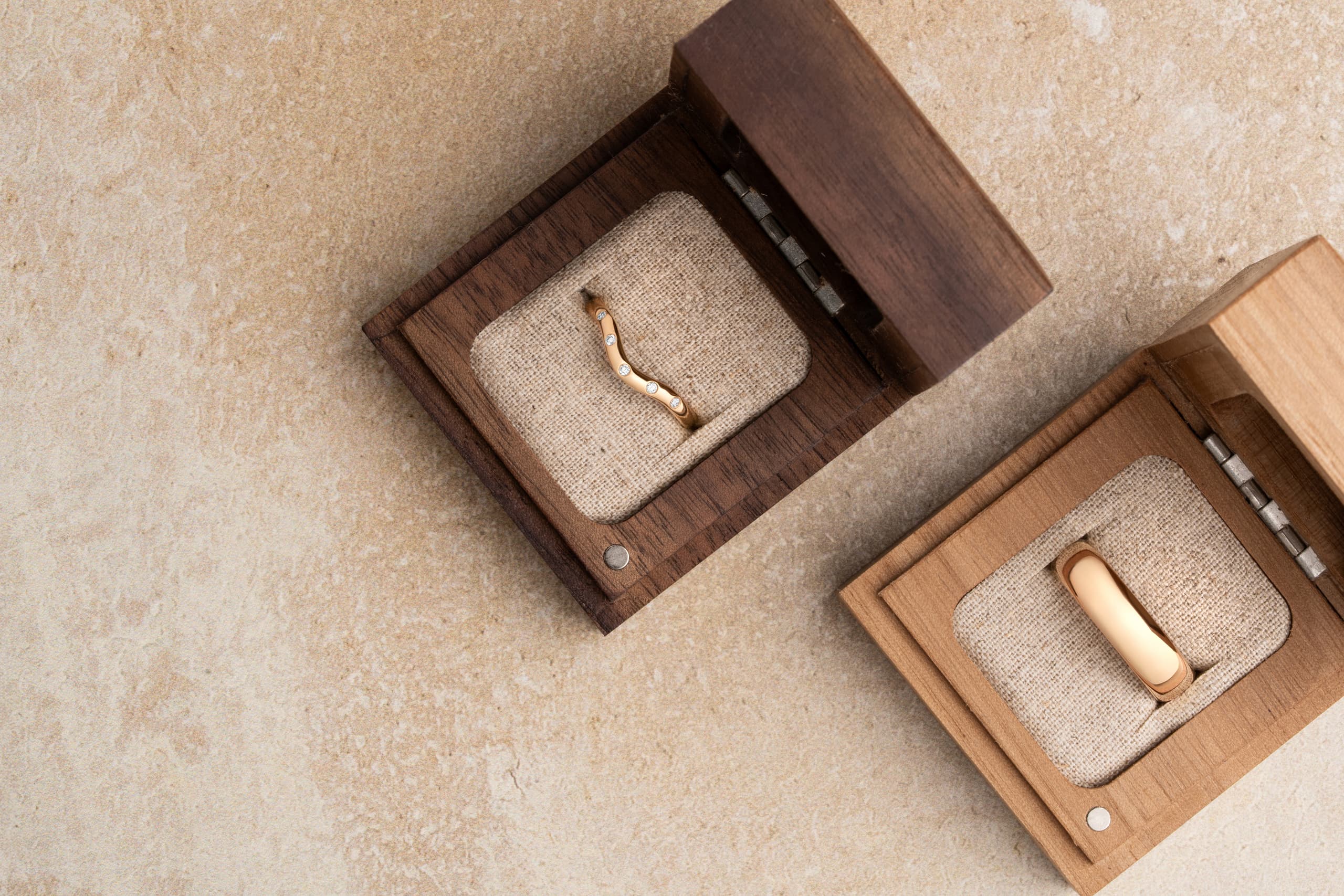 A rose gold diamond-set shaped wedding band and a plain rose gold wedding band in open wooden ring boxes