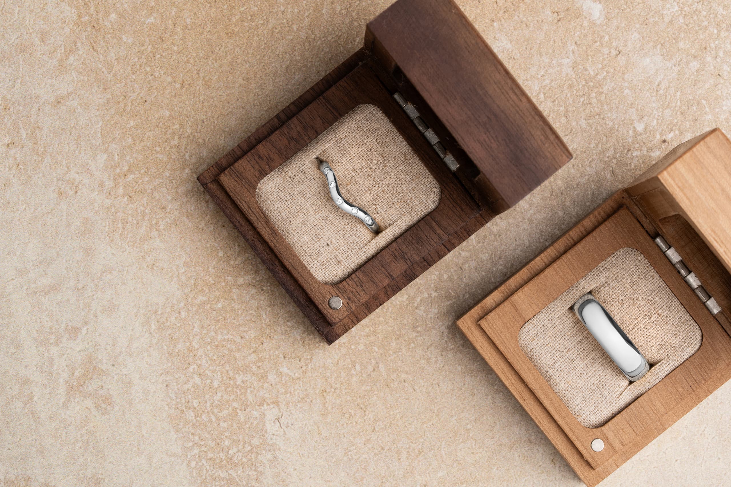 A white gold diamond-set shaped wedding band and a plain white gold wedding band in open wooden ring boxes